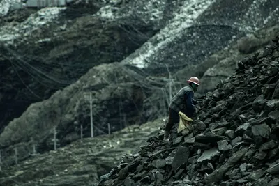 A solitary worker climbs a rocky slope in a barren quarry, wearing safety gear.