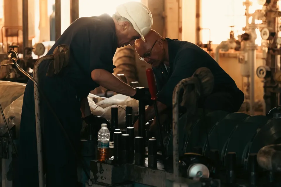 Two engineers collaborating on machinery maintenance in a dimly lit industrial plant.