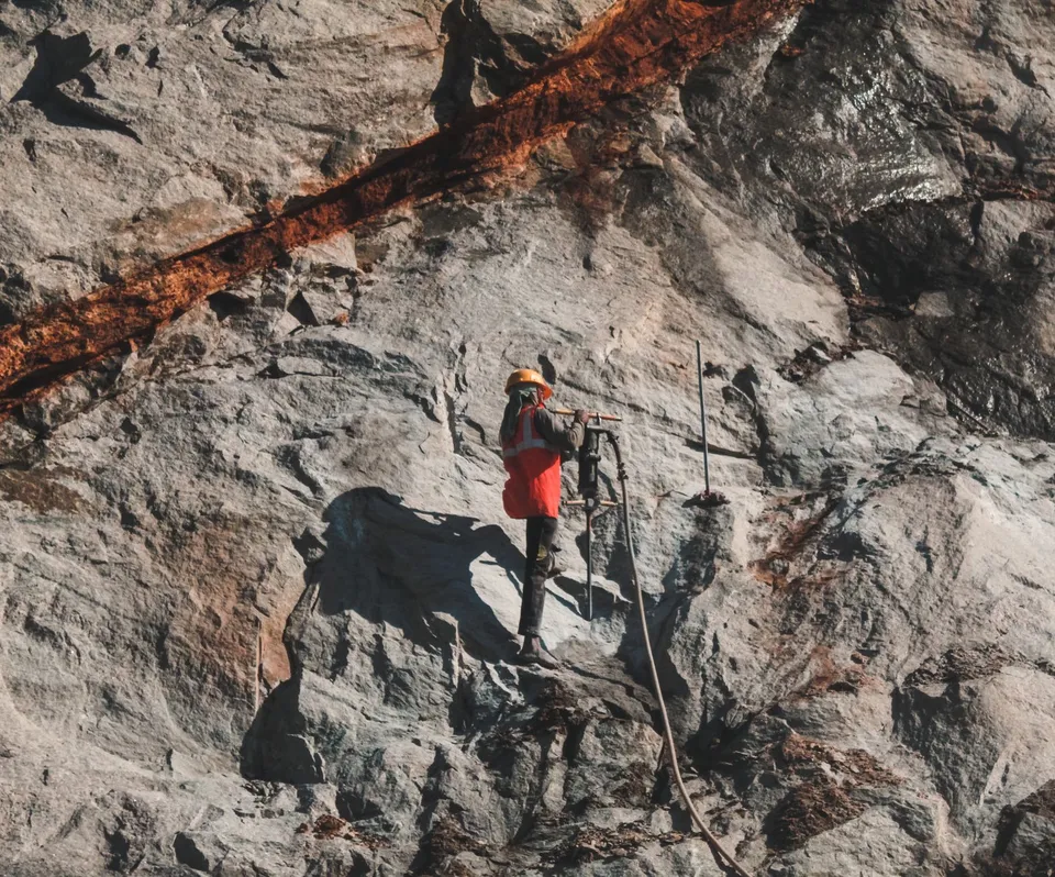 Construction worker drilling into rugged rock face, showcasing challenging outdoor work.