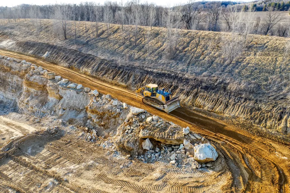 An aerial view of a bulldozer operating on a rocky terrain in a quarry setting during daylight.